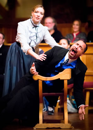 Dame Kitely, in Victorian white ruffled-front, high-lace-collared blouse and plain gray dress, has her hands on the shoulder and arm of Kitely in black suit with shiny blue vest, wailing with eyes closed as he leans over the back of a renaissance chair.